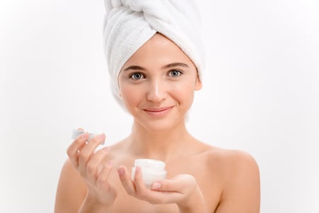 Beautiful young female with towel on her head using face cream over white background-1