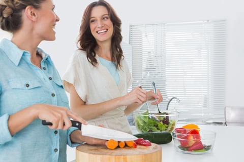 Cheerful women preparing salad together  in the kitchen