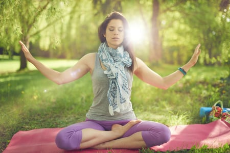 Serene and peaceful woman practicing mindful  awareness by meditating in nature with sun flare.-1