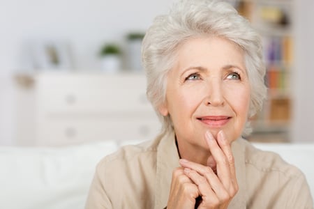 Thoughtful senior lady sitting at home with her fingers to her chin reminiscing and recalling fond memories, close up portrait