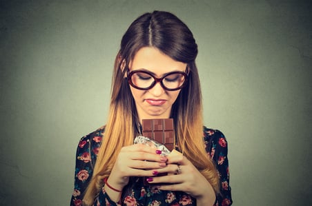 Portrait sad young woman tired of diet restrictions craving sweets chocolate isolated on gray wall background. Human face expression emotion. Nutrition concept. Feelings of guilt